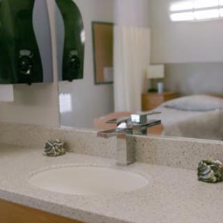 A modern bathroom sink with a sleek faucet, reflecting light and leading into a cozy bedroom.
