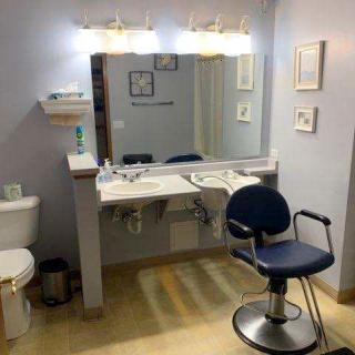 A bathroom setup with a large mirror, vanity sink, toilet, and a chair.
