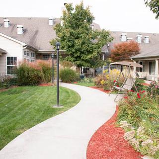 A beautifully landscaped garden with a winding pathway, benches, and a swing surrounded by lush greenery and trees.