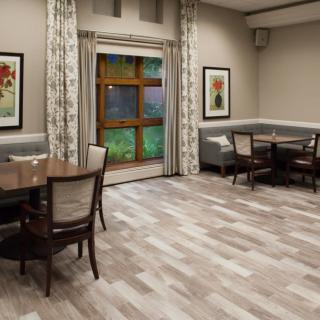 A cozy dining area with wooden floors, featuring tables, chairs, and decorative artwork on the walls.