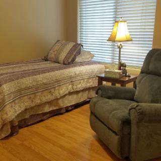 A cozy bedroom featuring a single bed, an armchair, and soft lighting.