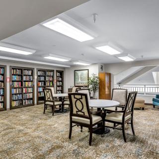 A cozy library setting with bookshelves, tables, and chairs under bright lighting.