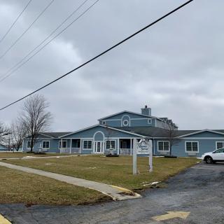A blue building with a parking lot and lawn under a cloudy sky.