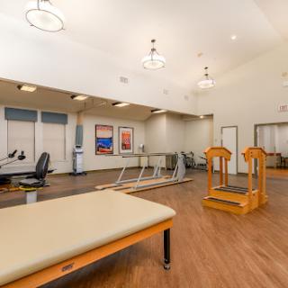 An interior view of a physical therapy facility, featuring exercise equipment and a therapy table.