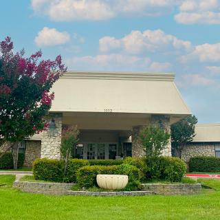 A building entrance surrounded by landscaping and trees under a cloudy sky.