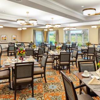 An elegantly set dining room with multiple tables and chairs, featuring warm lighting and large windows.