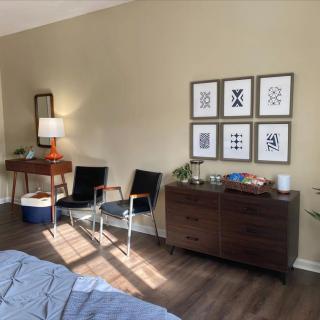 A stylish bedroom with a dresser, chairs, and framed artwork.