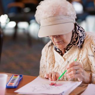 An elderly woman engaged in painting with watercolors.