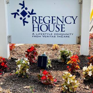 A sign for Regency House, a lifestyle community, surrounded by colorful flowers.