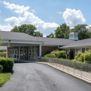 A building with a driveway leading to its entrance, surrounded by well-maintained landscaping, under a partly cloudy sky.