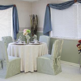 A cozy dining area with a round table and covered chairs, adorned with elegant window drapes.