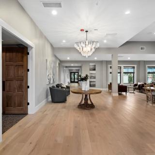 A spacious and modern interior with hardwood floors, featuring a chandelier, table, and chairs in a well-lit living area.