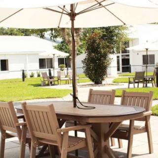 A sunny patio area with a wooden table and chairs under an umbrella.