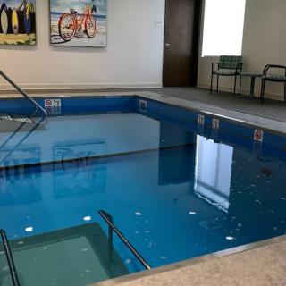 An indoor therapy pool with exercise equipment and chairs by the side.
