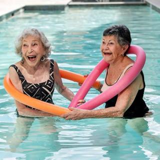 Two elderly women enjoying a fun time in the swimming pool with pool noodles.
