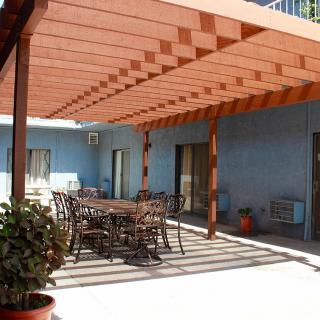 An outdoor patio area with a wooden pergola providing shade over a dining set.