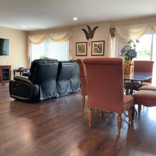 A cozy living room with a dining area, featuring a black leather sofa, hardwood flooring, and large windows allowing natural light.