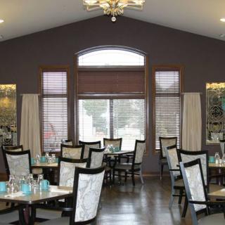 A spacious restaurant dining room with elegantly arranged tables and chairs, featuring a large window and chandelier.