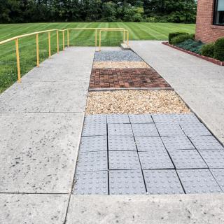 An outdoor walkway featuring various textured sections, including concrete, pavers, and stones.