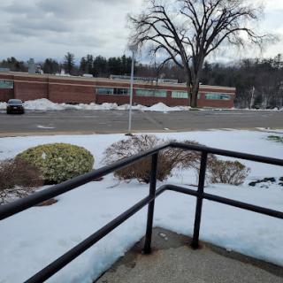 A winter scene showing a snowy landscape with a tree and a building in the background.
