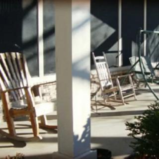A sunlit porch with rocking chairs casting shadows on the ground.
