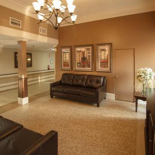 A cozy living room with brown tones, featuring leather sofas, framed artwork, and a chandelier.