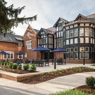 A beautifully restored historic building with Tudor-style architecture, featuring outdoor seating and landscaped surroundings.