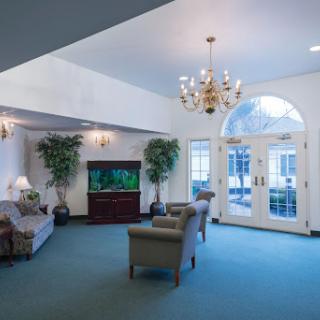 A cozy lobby area featuring comfortable seating, a television, and decorative plants, illuminated by a chandelier.