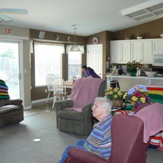 A cozy living room with elderly individuals seated in chairs, showcasing a home-like atmosphere.