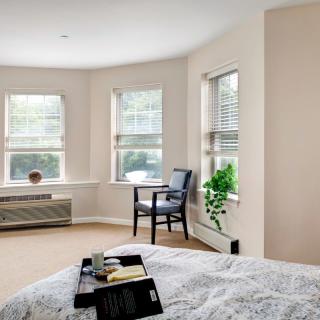 A bright and airy bedroom with large windows, a cozy chair, and neutral decor.