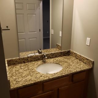 A bathroom with a granite countertop and an oval sink beneath a mirror.