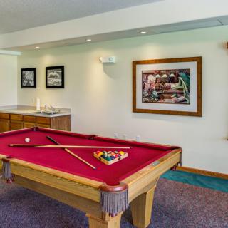 A cozy game room featuring a pool table with red felt, framed artwork on the walls, and ambient lighting.