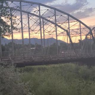A beautiful sunset illuminating an old bridge framed by mountains and lush greenery.
