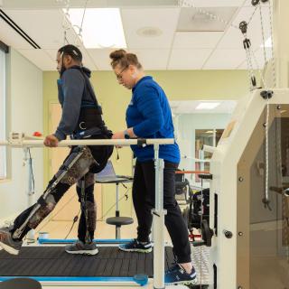 A healthcare professional assists a patient using an exoskeleton on a treadmill in a rehabilitation setting.