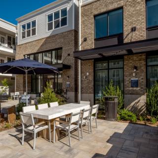 A modern outdoor patio featuring a dining set with an umbrella, surrounded by greenery.