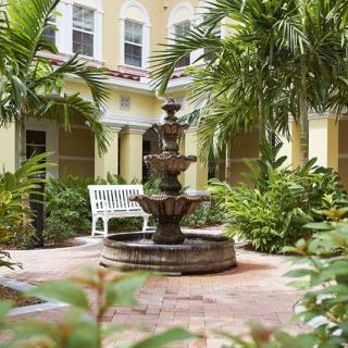 A tranquil courtyard with a central fountain surrounded by tropical plants and palm trees.