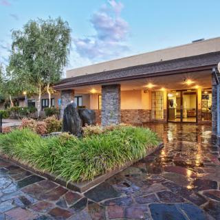 A welcoming hotel entrance surrounded by lush landscaping and a reflection on the wet pavement.