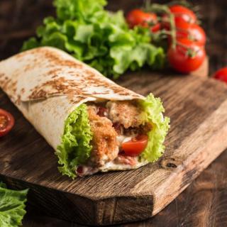 A delicious chicken wrap with lettuce and tomatoes on a wooden board.