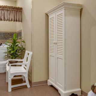 A bathroom with a white wardrobe, plastic chair, and a potted plant.