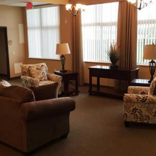 A cozy living room with upholstered chairs, a sofa, tables, and lamps near large windows.