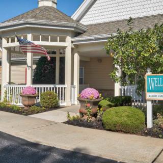 A welcoming building entrance with a flag, well-maintained landscaping, and a sign.