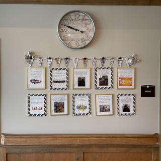 A decorative wall with a clock and an arrangement of framed photos and artwork.