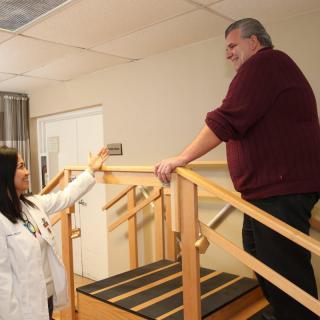 A healthcare professional assists a patient with physical therapy exercises on a staircase.
