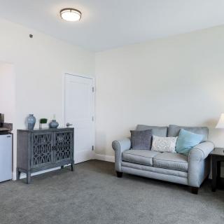 A cozy living room with a gray sofa and decorative pillows, accompanied by a side table with a lamp and a stylish cabinet.
