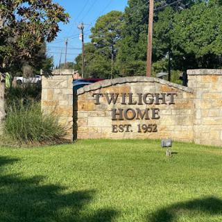 Entrance sign of Twilight Home, established in 1981, surrounded by green grass and trees.