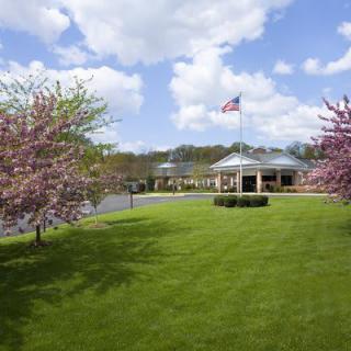 A scenic view of a building with an American flag, surrounded by blooming trees and a green lawn under a cloudy sky.