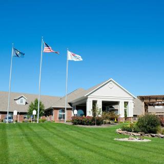 A well-maintained building with a lush green lawn and flags waving against a clear blue sky.