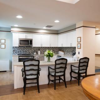 A modern kitchen with a sleek design featuring a white countertop, stylish bar stools, and stainless steel appliances.