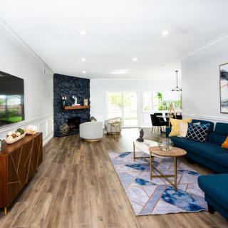 A modern and spacious living room featuring a blue sofa and hardwood floors, with an open concept dining area and fireplace.