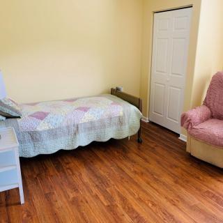 A simple bedroom featuring a single bed, hardwood flooring, and a cozy chair.